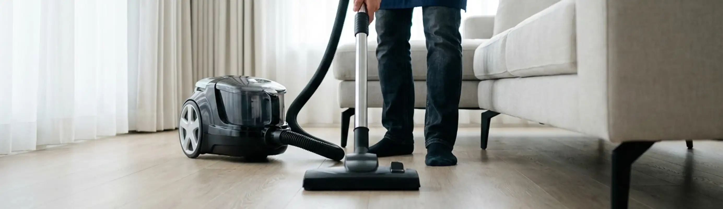 Professional house cleaner vacuuming a living room floor with a canister vacuum cleaner, Denver, CO.