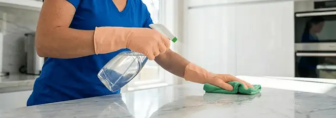 Maid service worker spraying and wiping a kitchen countertop with a microfiber cloth for sanitizing, Denver, CO.