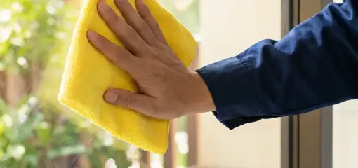House cleaner wiping a glass window with a yellow microfiber cloth for streak-free cleaning, Denver, CO.